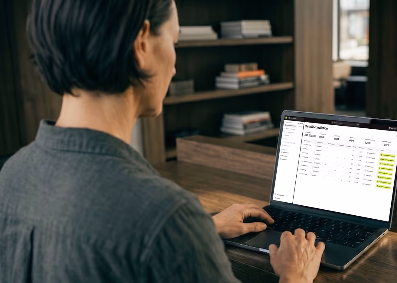Person using a laptop showing a bank reconciliation screen with transaction details and statuses.