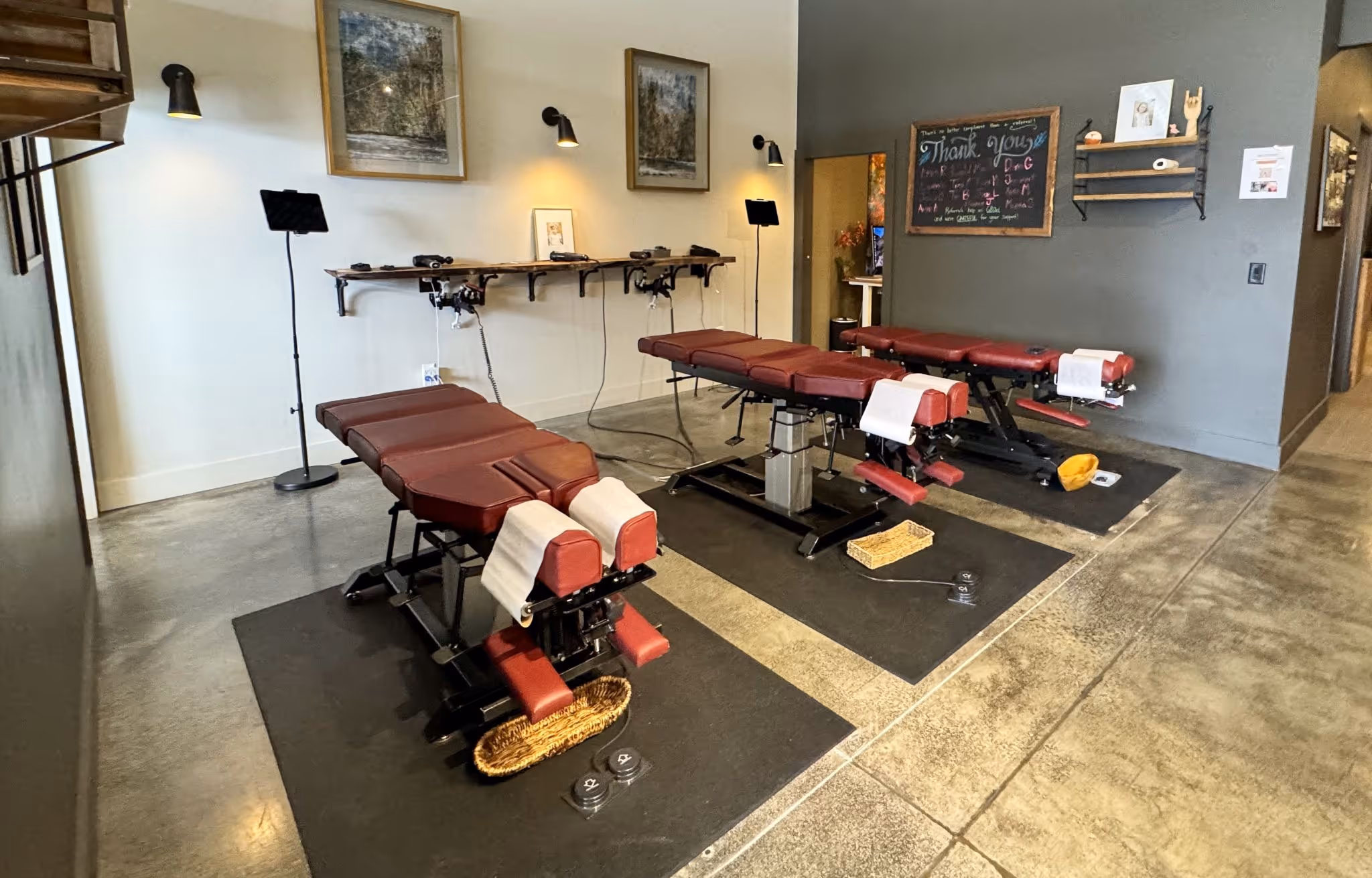 Treatment room with three chiropractic adjustment tables, wall-mounted equipment, and modern décor in a clean, open clinical space.
