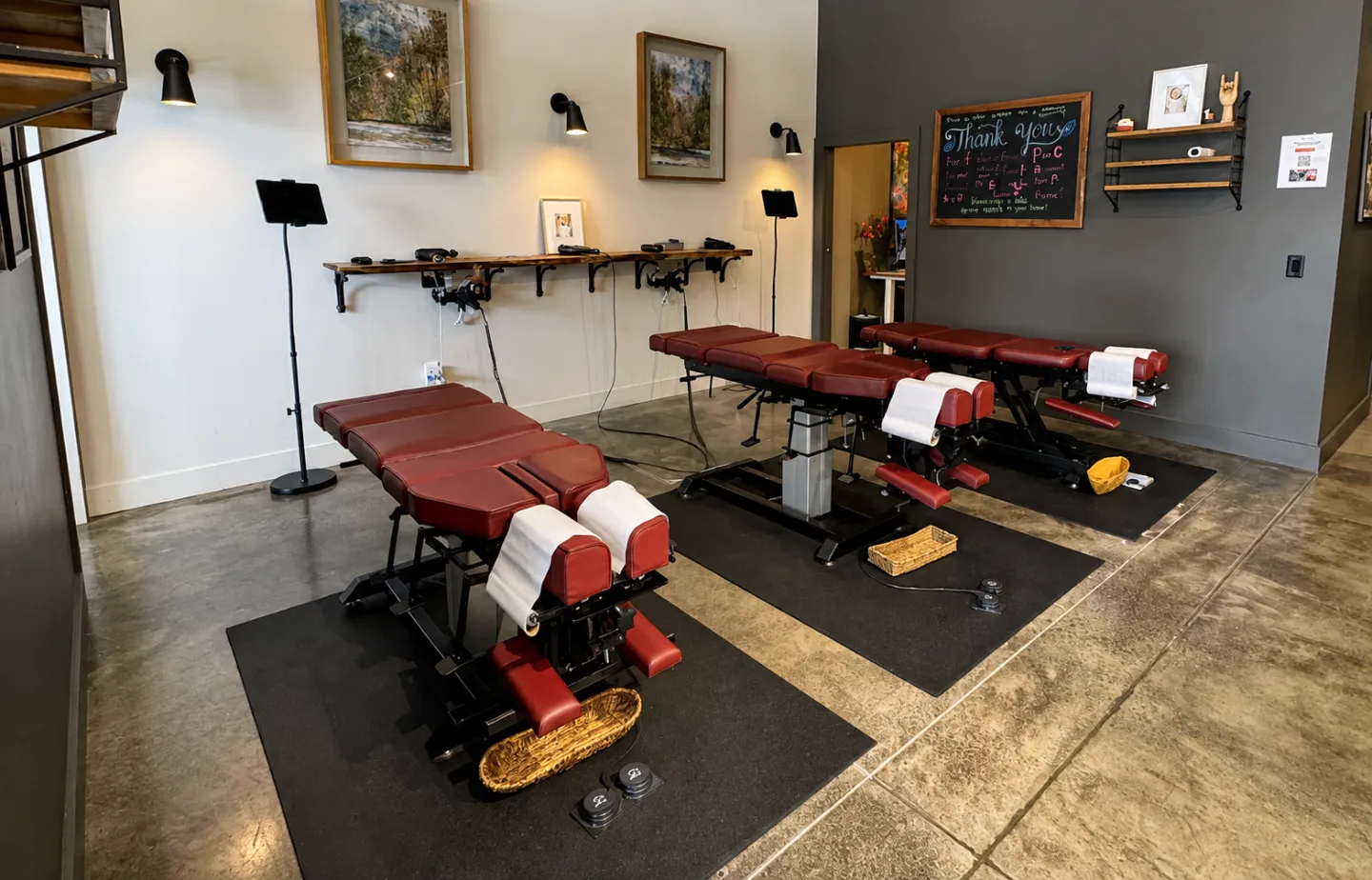 Chiropractic treatment room at Thrive Wellness Center with several adjustable treatment tables and rehabilitation equipment