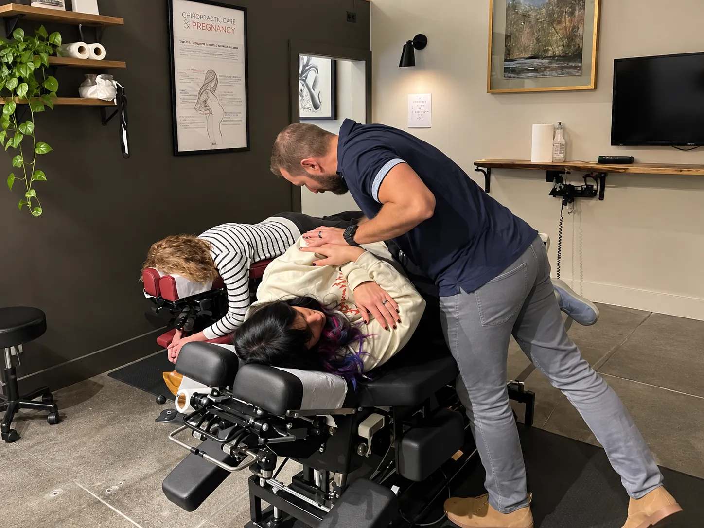 Dr. Ben Ozanne performing an adjustment on a patient positioned on a specialized chiropractic treatment table in a clinical setting.