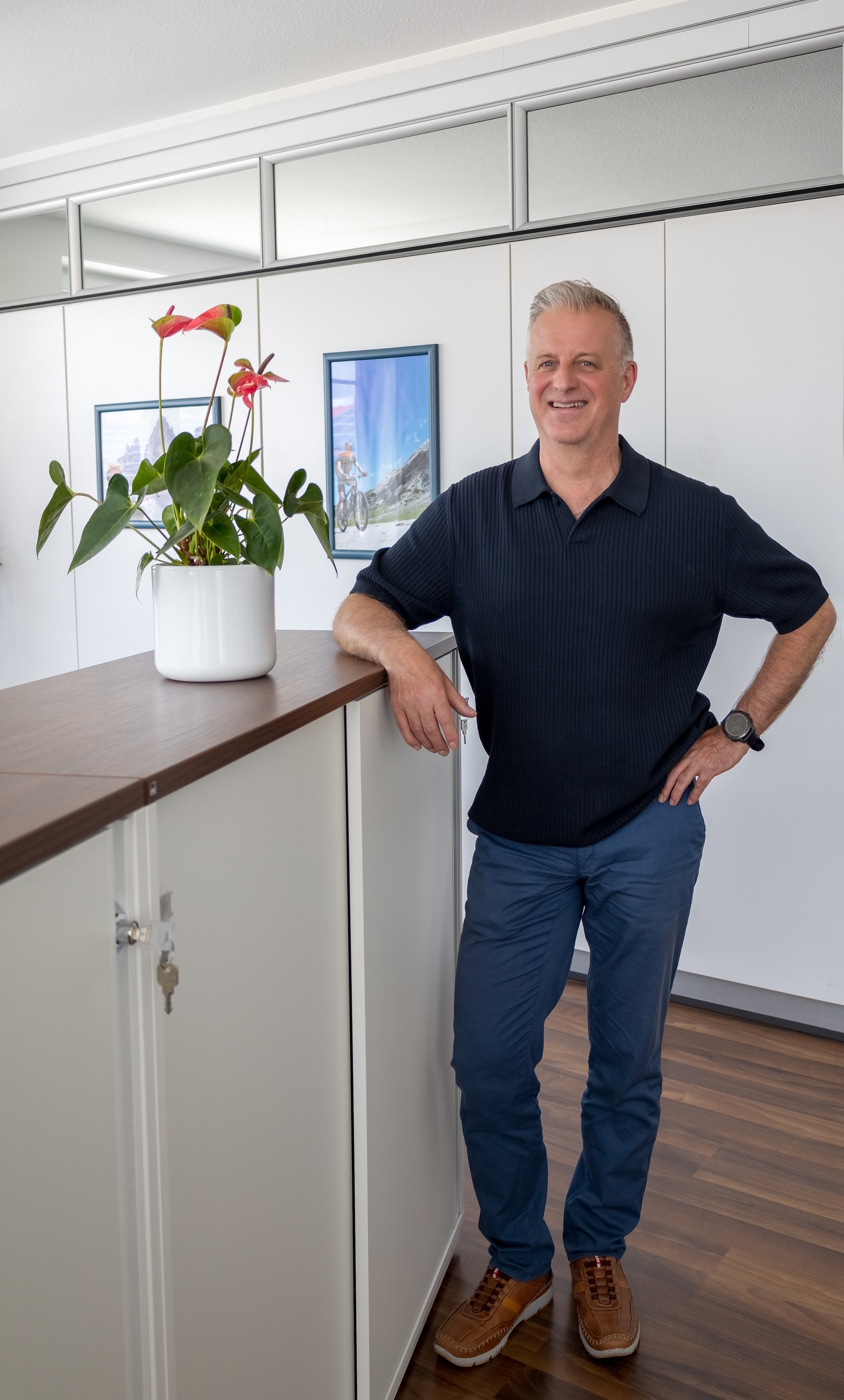 Mann lehnt lächelnd an einem weißen Schrank mit einem Blumentopf im Innenraum.