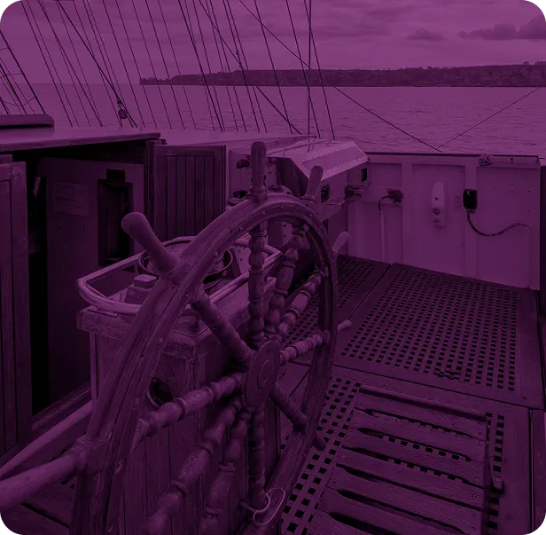 Gouvernail en bois sur le pont d'un voilier avec la mer et une côte rocheuse en arrière-plan.