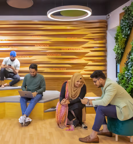 Four diverse professionals collaborate in a modern, creative office space with wooden wall design, indoor plants, and circular lighting; part of a career promotion for Musemind.