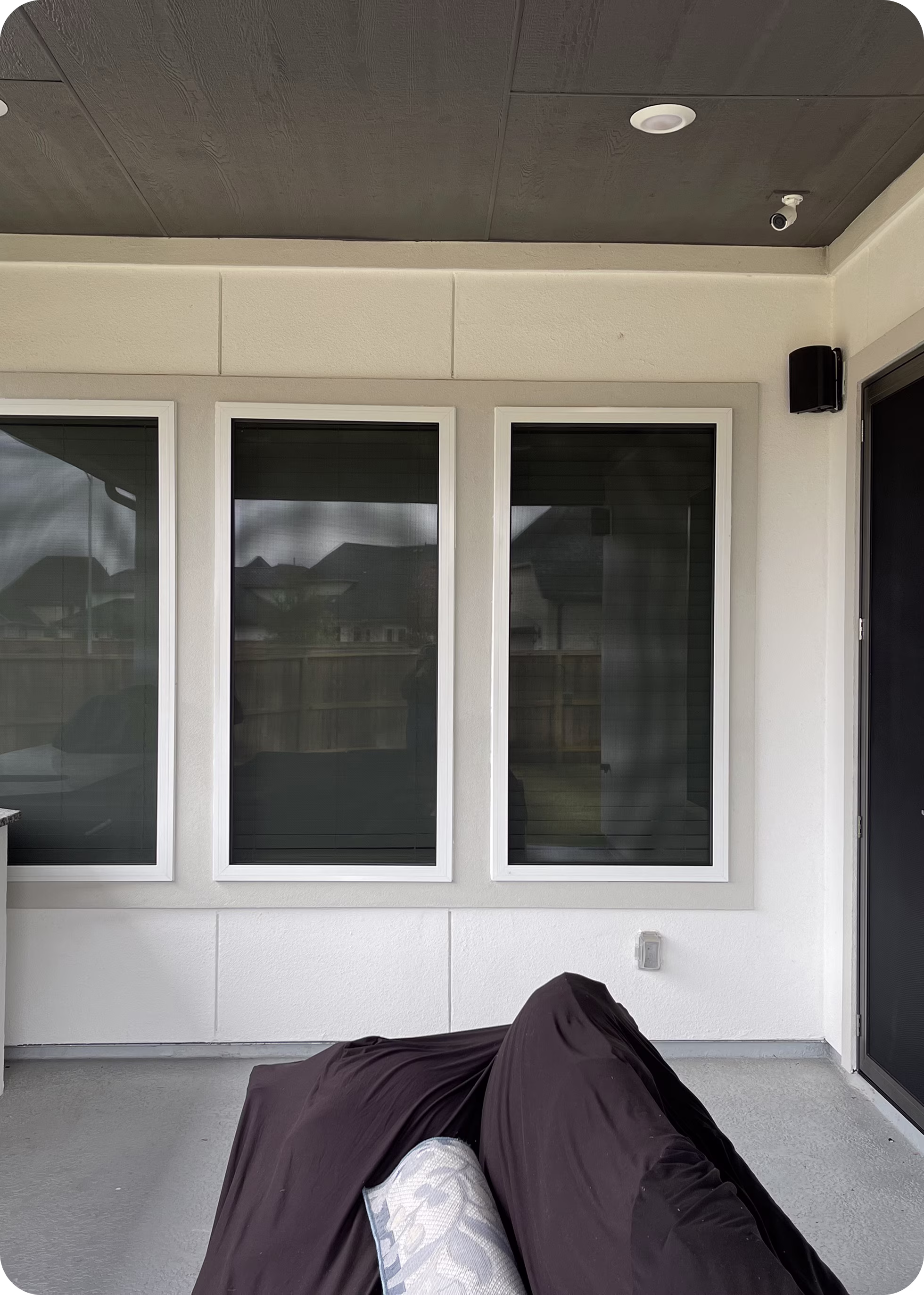 Covered outdoor furniture in a patio area with three large windows and a door on a cream-colored wall.