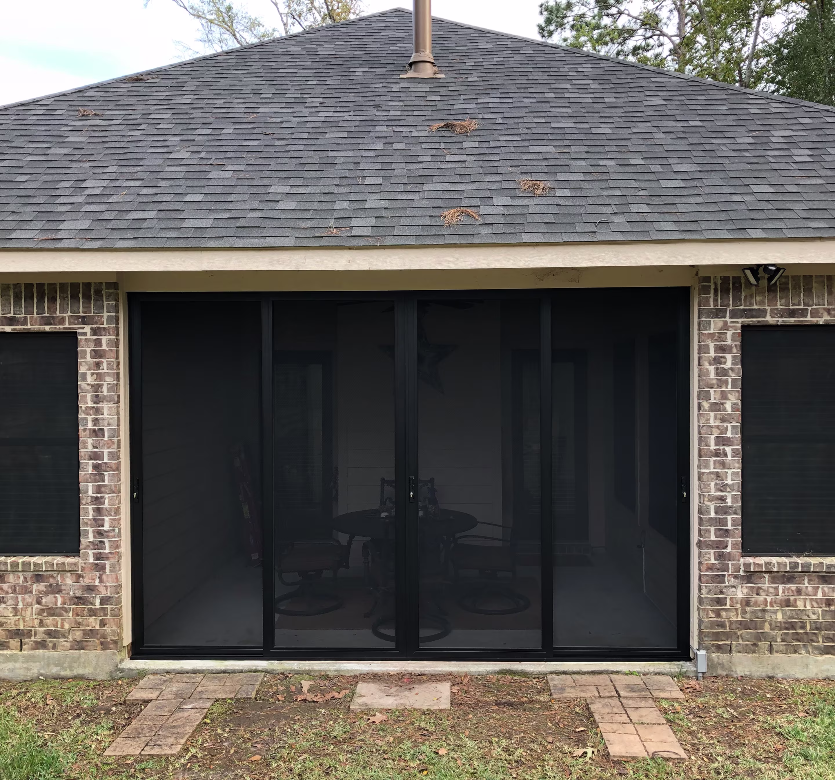 A brick house exterior with a screened-in patio door showing a round table and chairs inside.