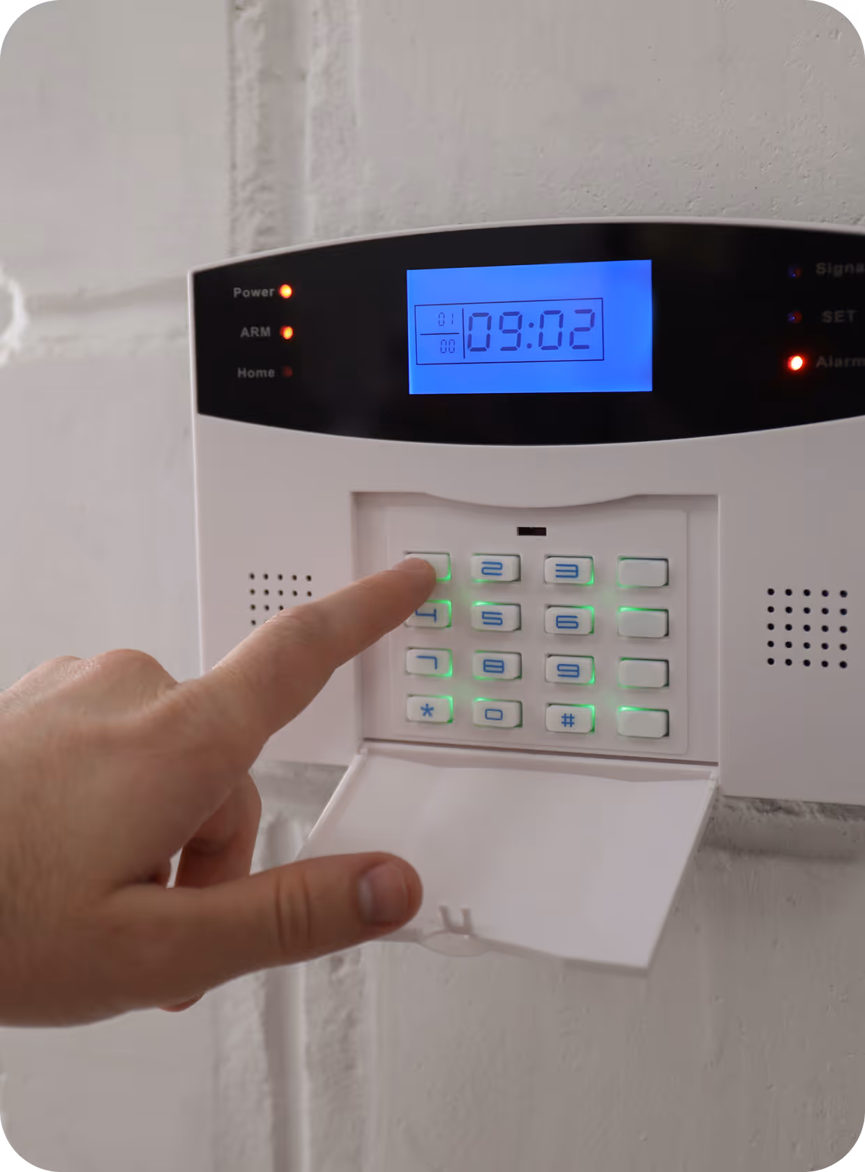 Hand pressing the number 1 on a home security alarm keypad with a blue digital display showing the time 09:02.