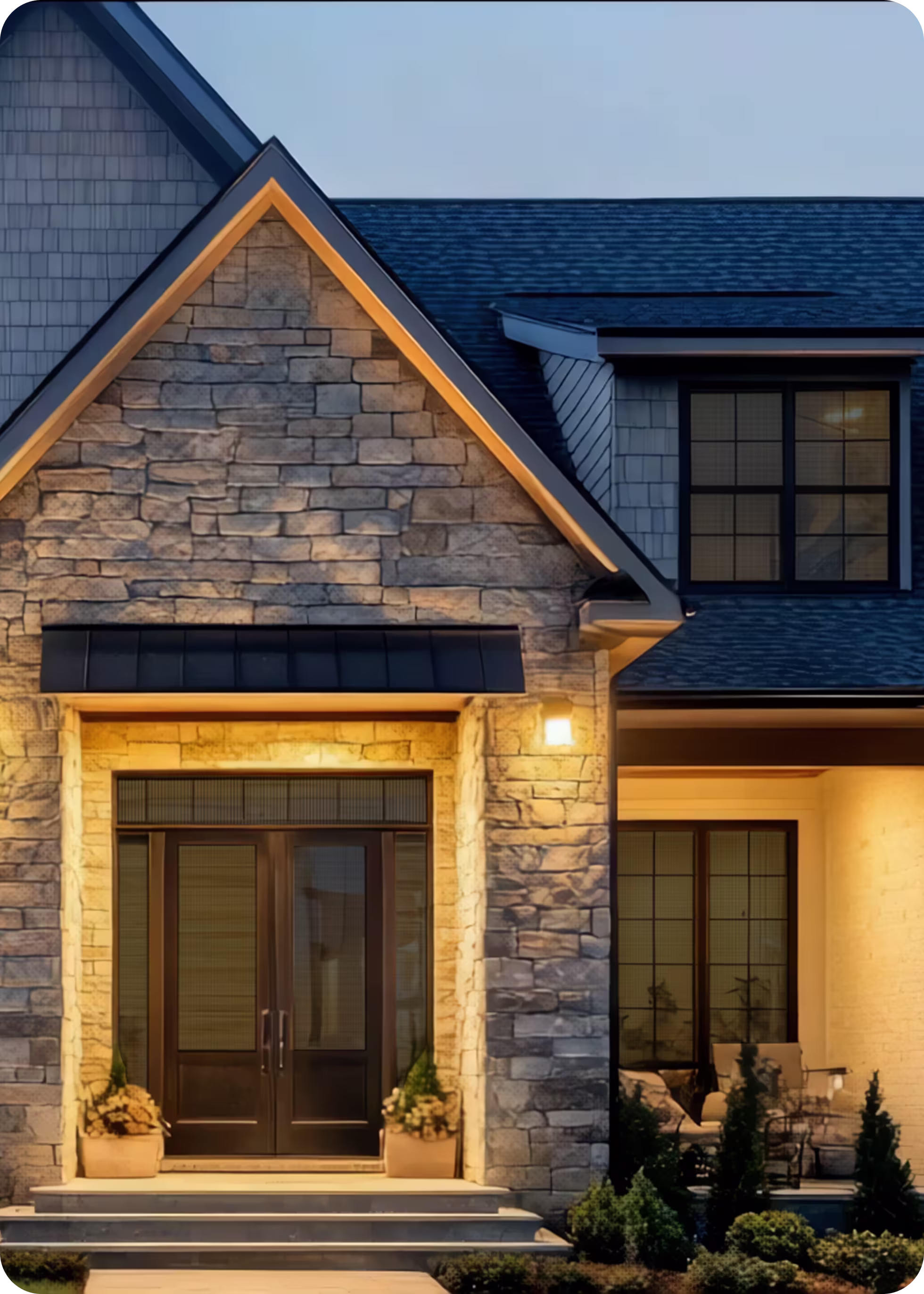 Stone house entrance with black double doors, warm exterior lighting, and potted plants on steps.
