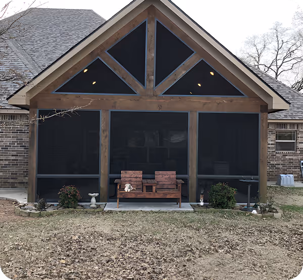 Back view of a brick house with a screened porch and a wooden bench in the center, surrounded by bushes and garden ornaments.