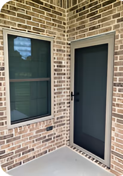 Corner of a brick patio with a window and a closed screen door with gray frames.