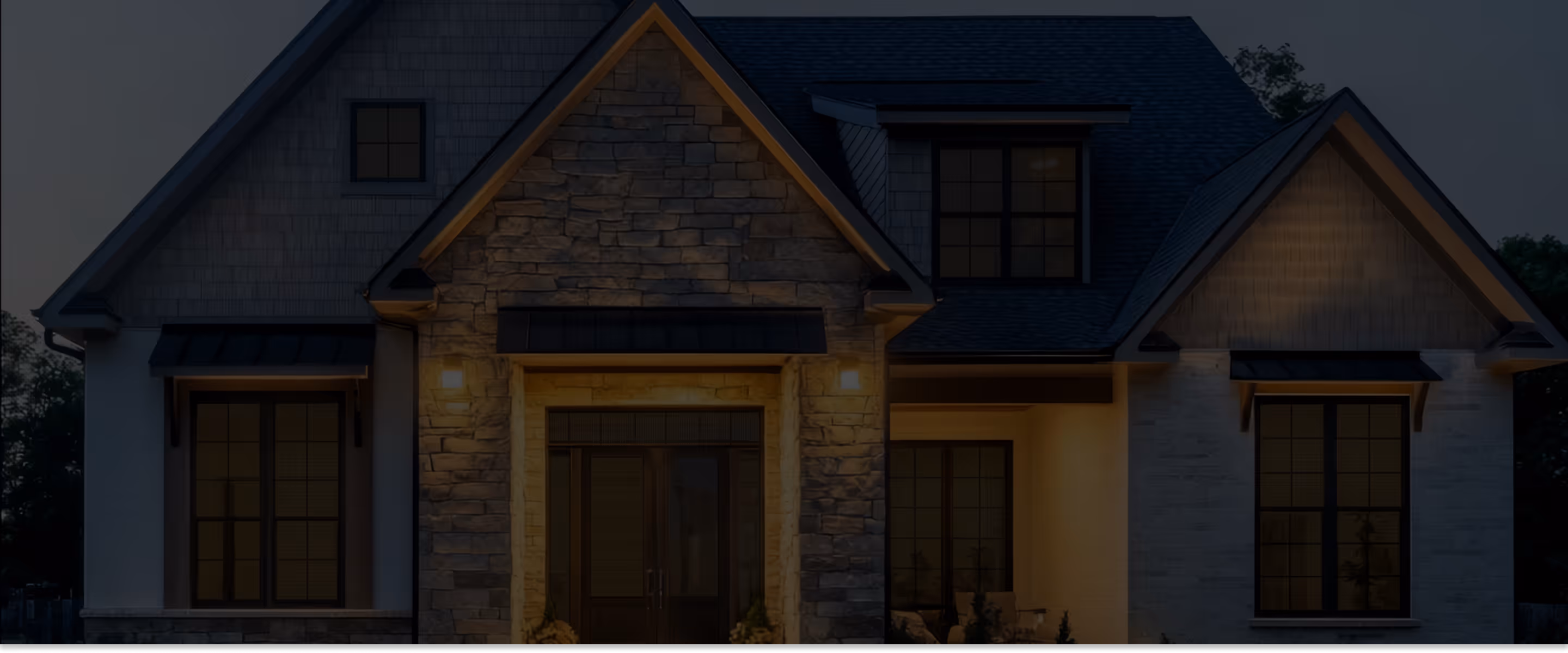 Modern house exterior at dusk with stone facade, large windows, and warm porch lights.