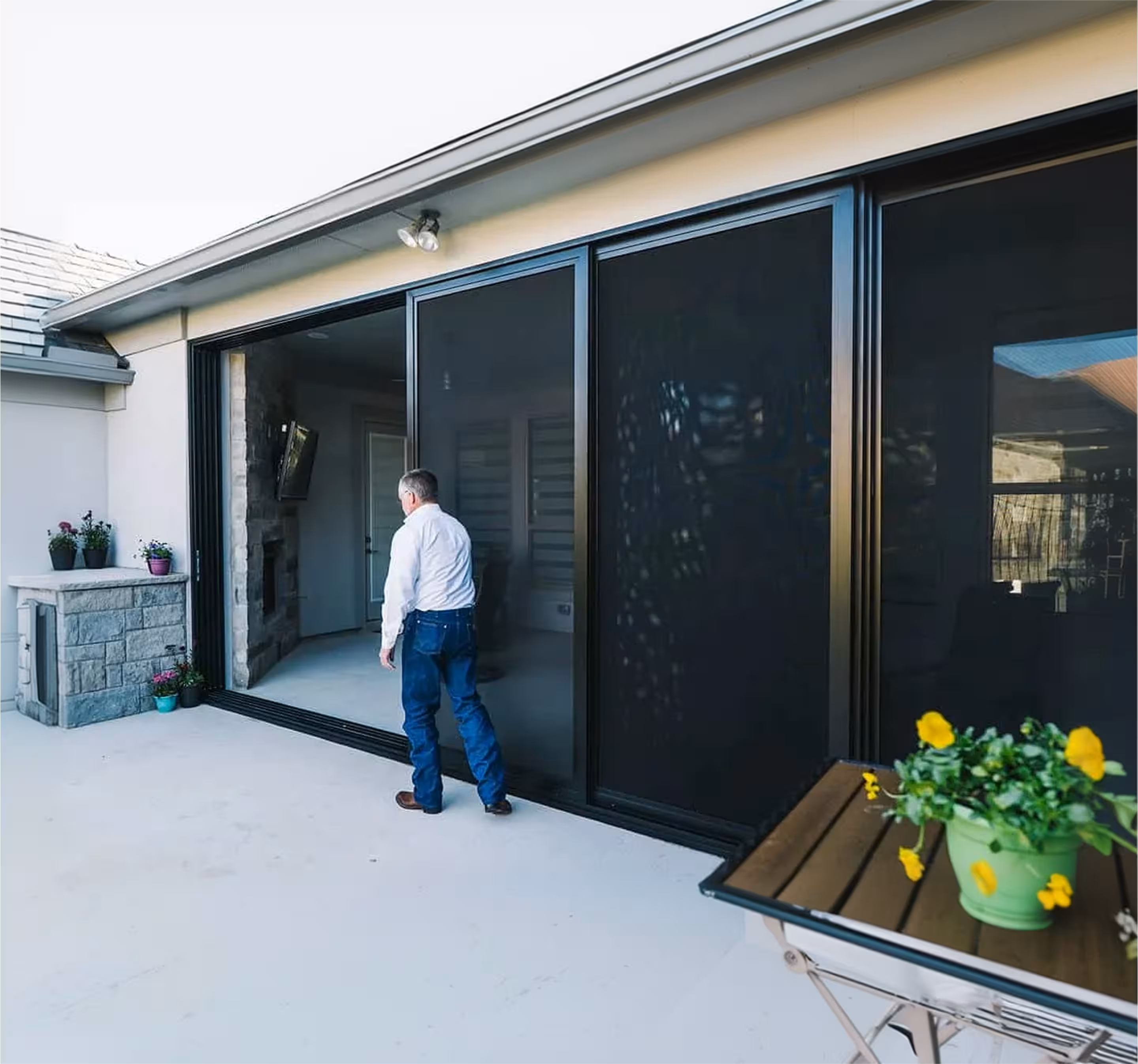 Man in a white shirt and blue jeans walking toward an open large sliding glass door leading into a home patio area.