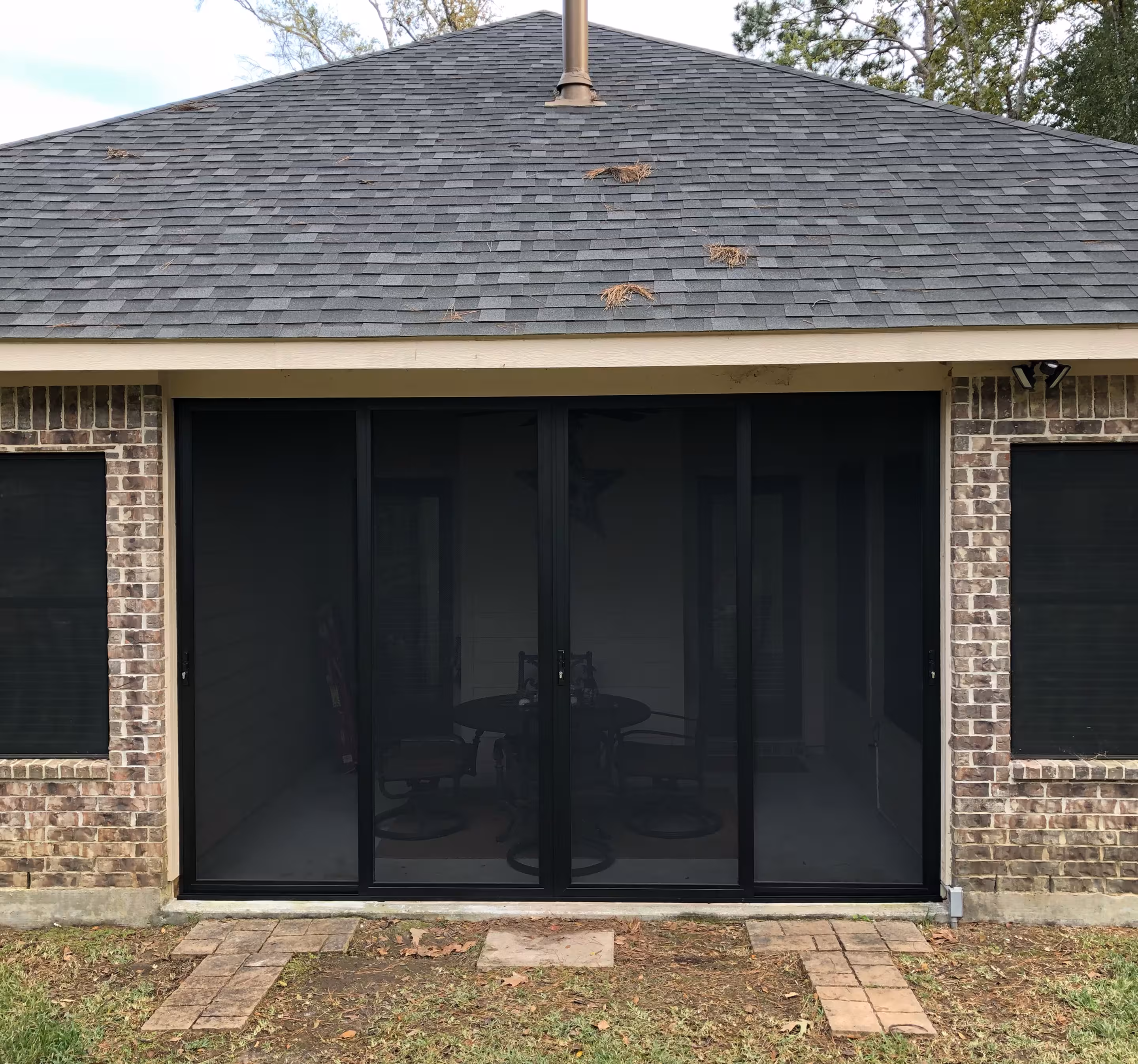 Brick patio house exterior with black framed sliding screen doors leading to a covered patio area with outdoor furniture.