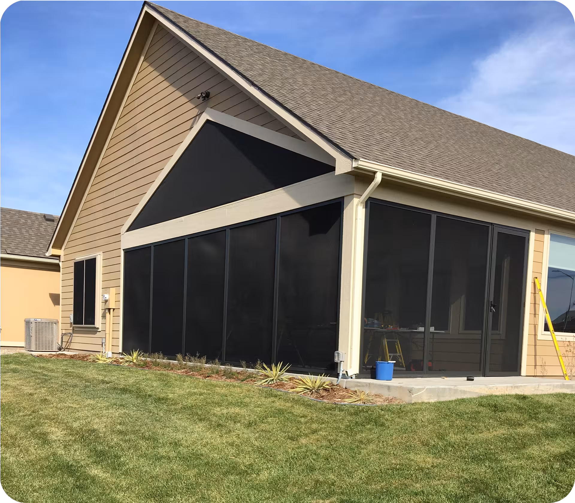 Modern house with a large screened-in porch on a well-maintained lawn under a blue sky.