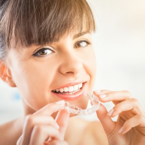 Smiling woman holding a clear dental aligner near her mouth.