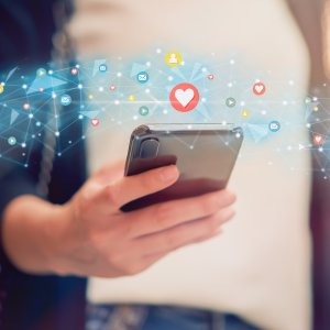 Person holding smartphone with floating social media icons and digital network connections.
