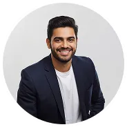 Smiling man with dark hair and beard wearing a navy blazer and white shirt against a light gray background.