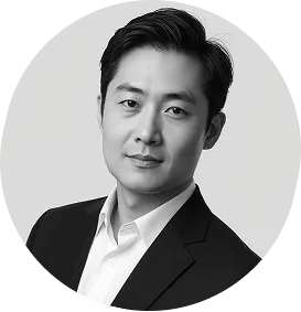 Headshot of a man with dark hair wearing a white shirt and dark blazer, against a light background.