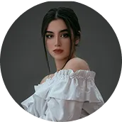 Portrait of a young woman with dark hair styled back, wearing an off-shoulder white blouse against a dark background.