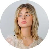 Young woman with blonde hair and light makeup wearing a lace top and heart-shaped necklace, looking to her right.