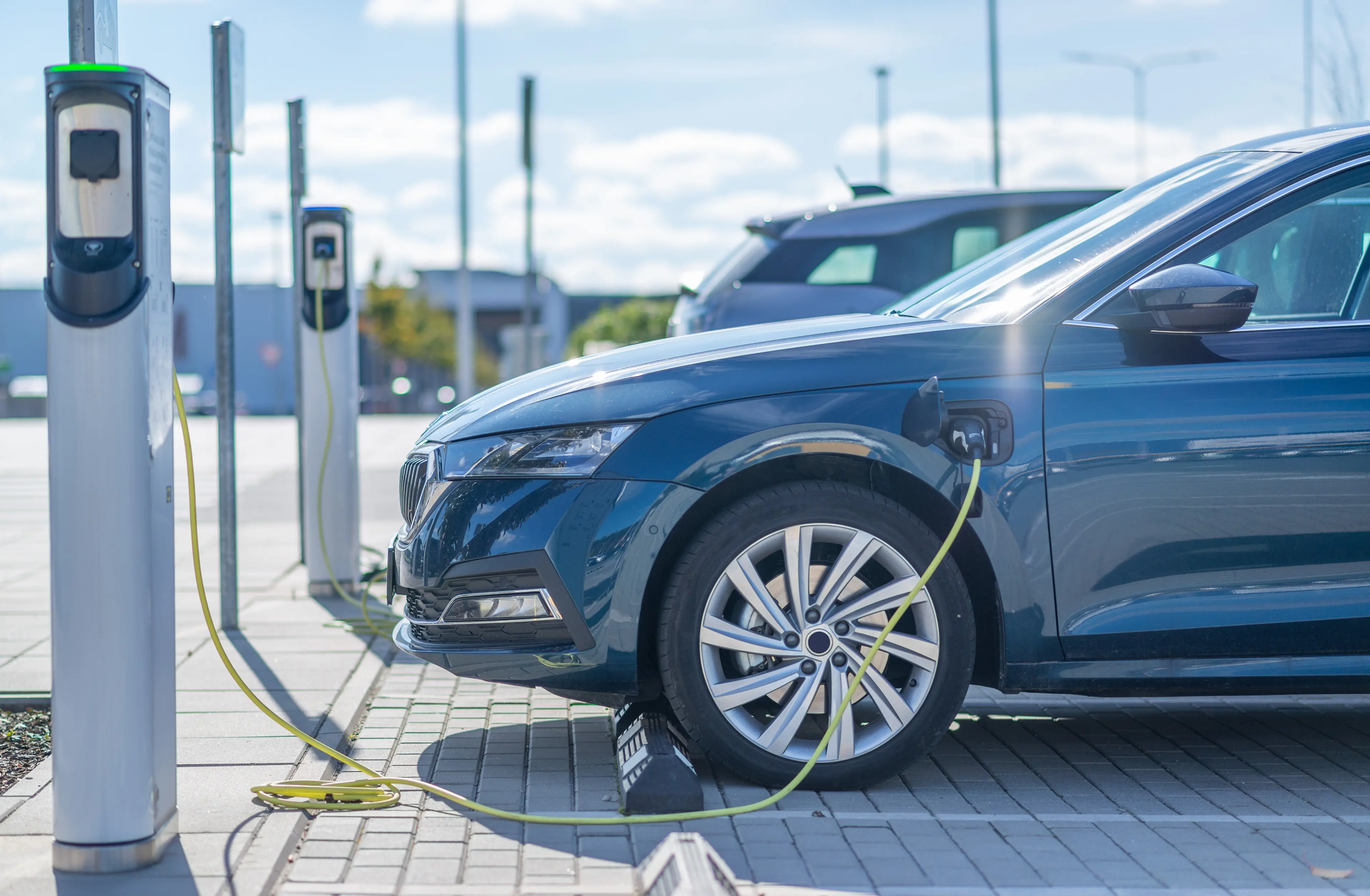 Blue electric car charging at a public charging station on a sunny day.