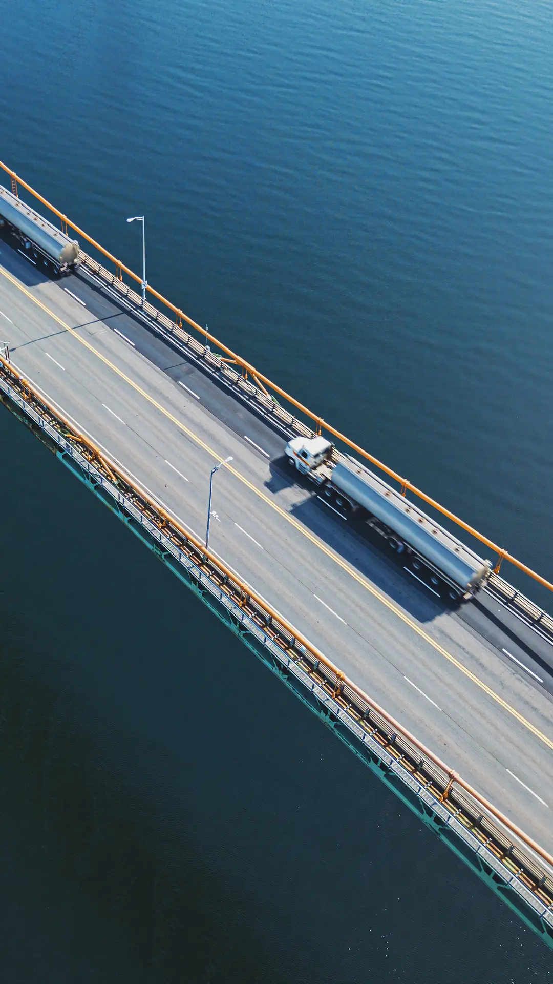 Aerial view of a bridge over calm water with two tanker trucks driving in opposite directions.