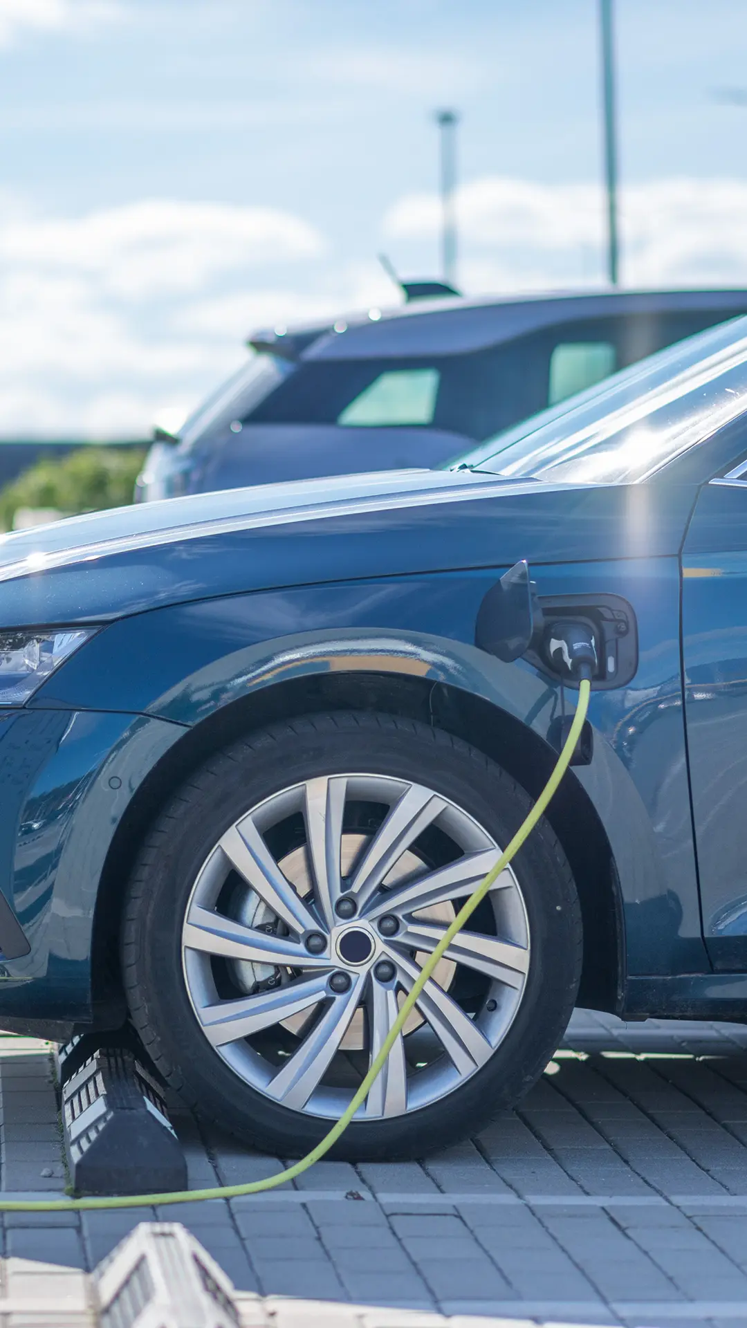 Blue electric car parked and connected to a charging station by a green charging cable.