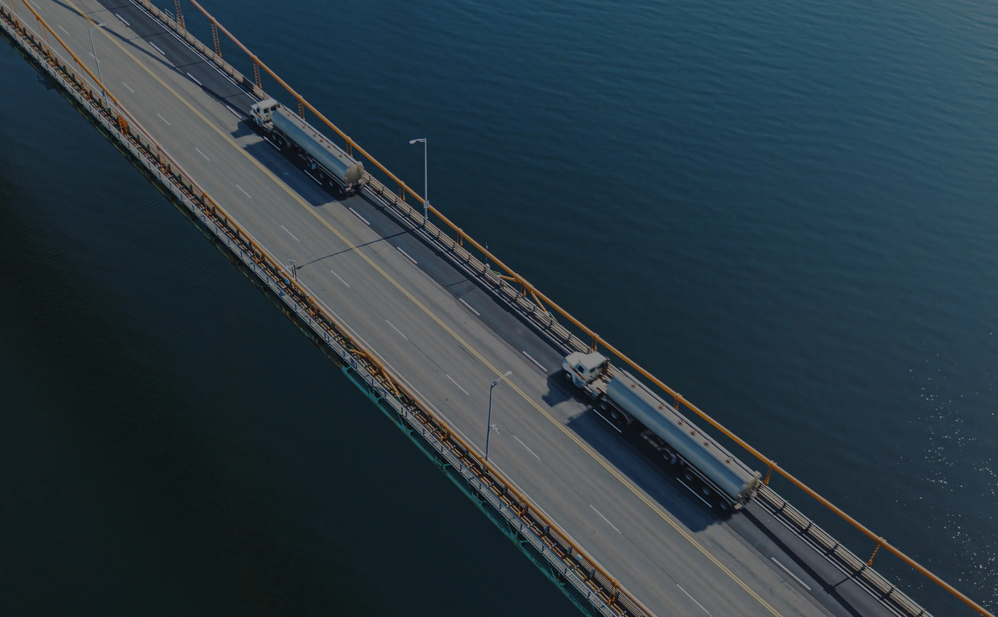 Aerial view of a bridge over water with two large tanker trucks traveling in opposite directions.