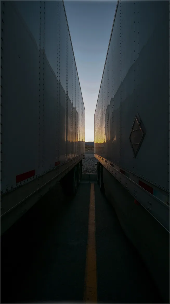 Narrow view between two parked white trailers at sunset with a yellow parking line on the ground.