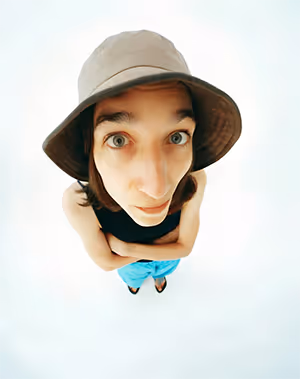 Person wearing a bucket hat looking up with a fisheye lens distortion against a light background.