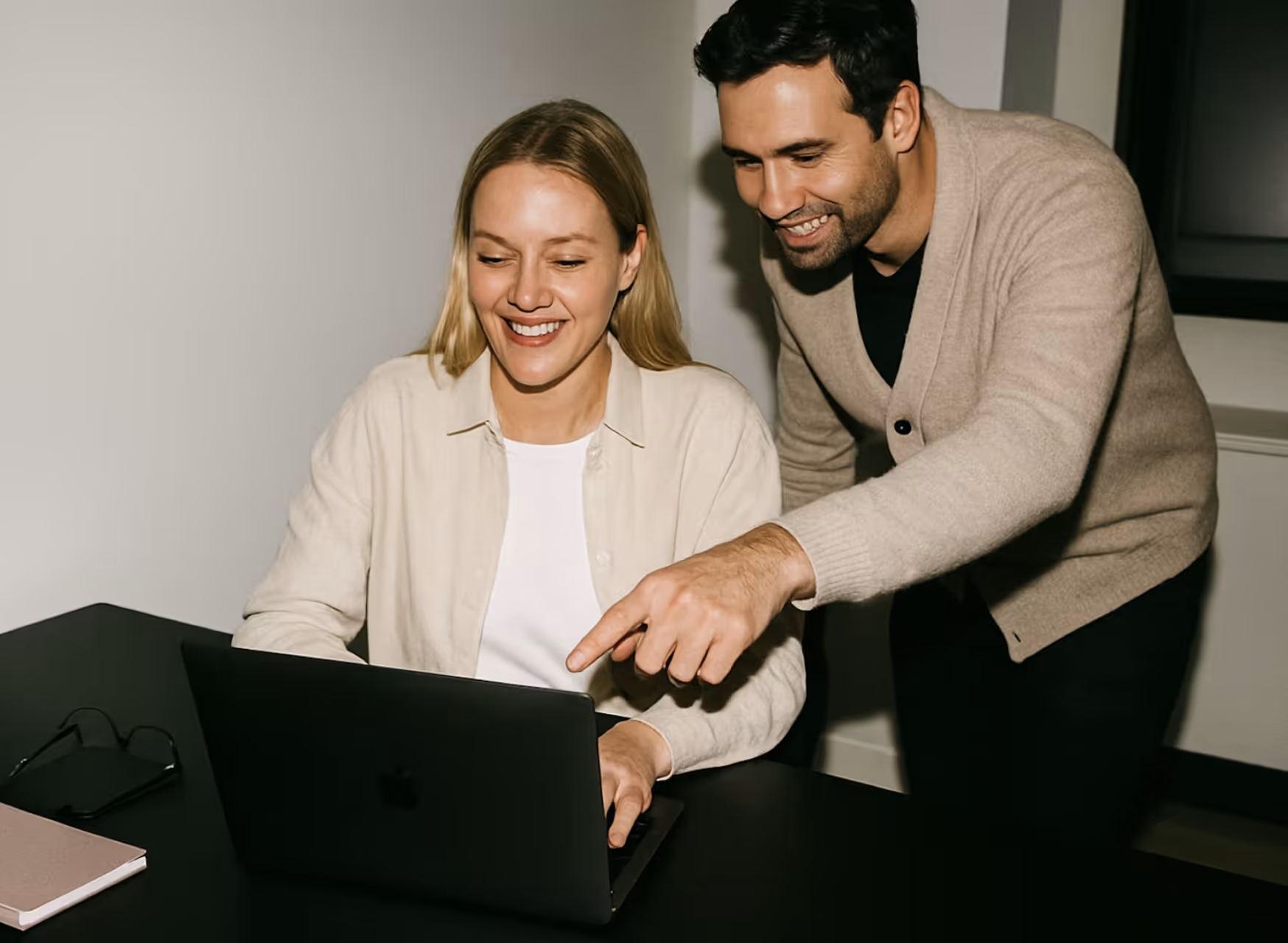 Smiling man and woman working together on a laptop at a desk indoors.