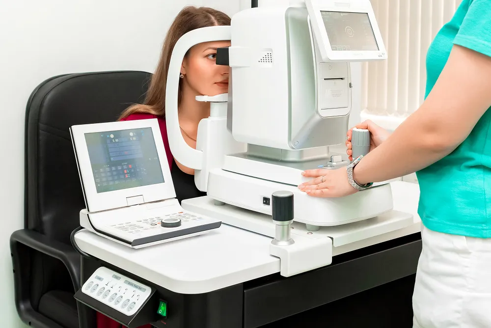 Woman undergoing an eye exam using an automated ophthalmic device operated by a healthcare professional.