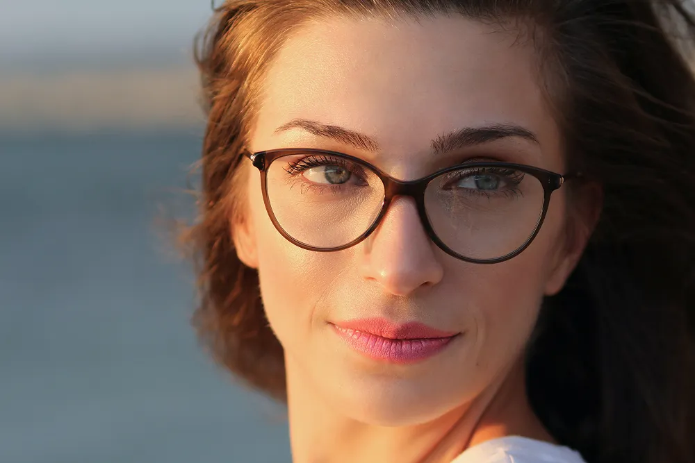 Close-up of a woman with brown hair and glasses looking to the side in natural light.