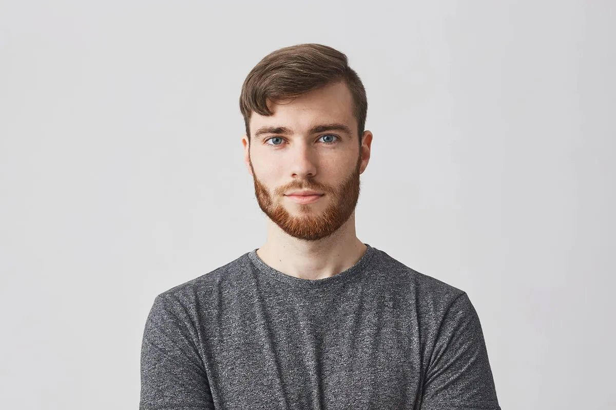 Portrait of a young man with light skin, blue eyes, short brown hair, and a red beard wearing a gray shirt.