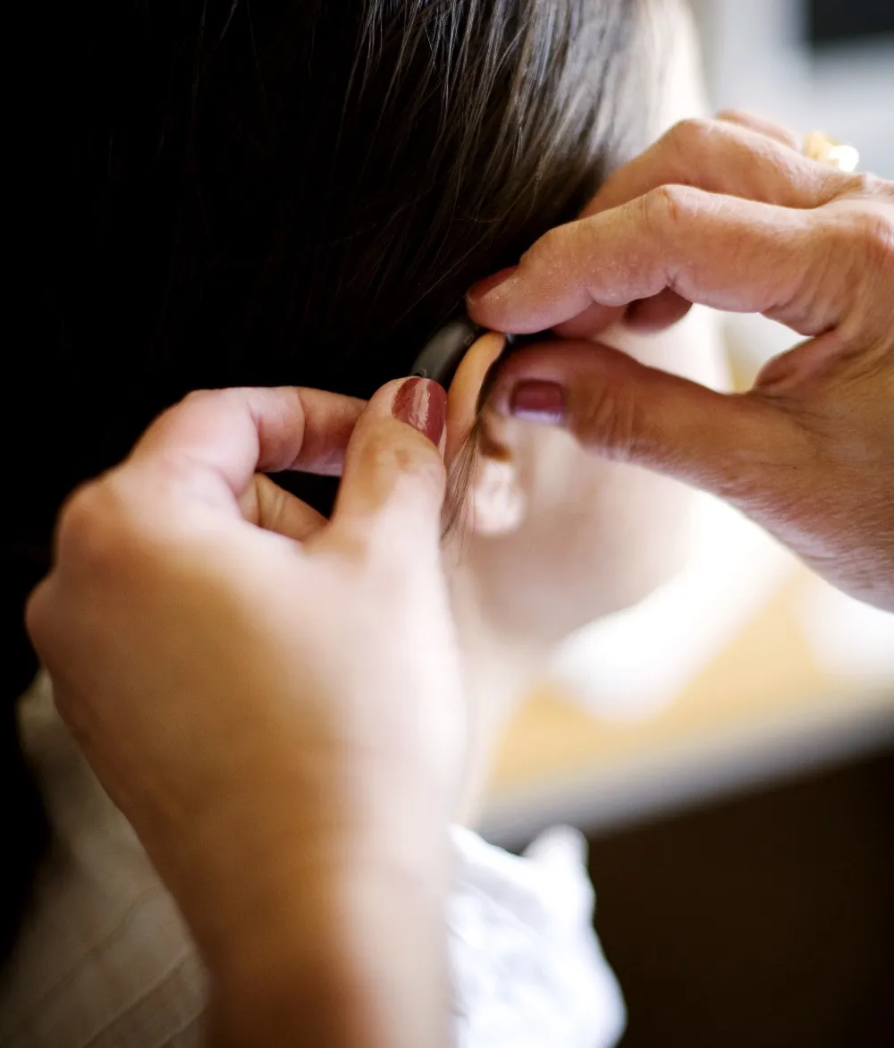 Close-up of hands adjusting a hearing aid behind a person's ear.