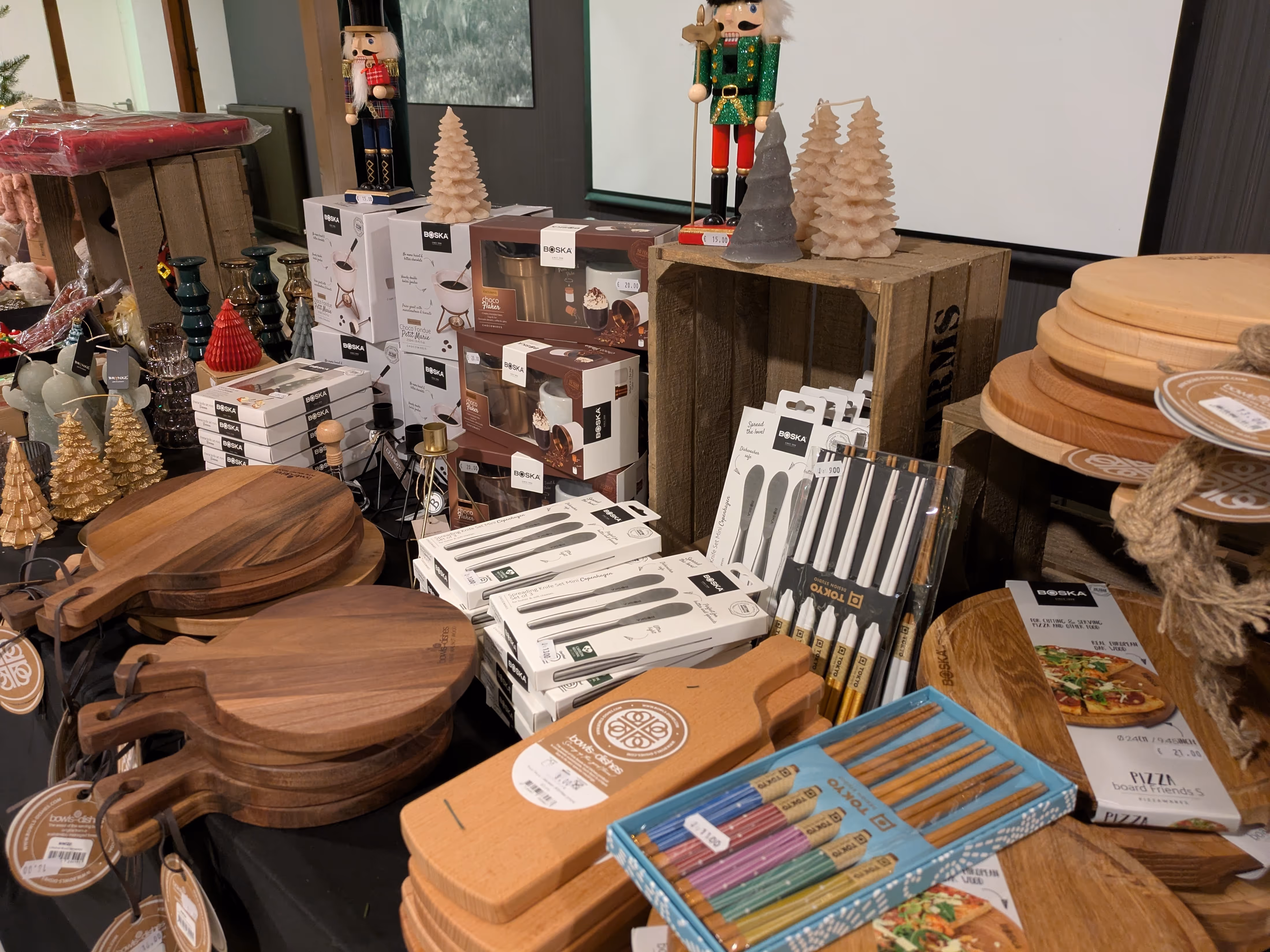 Tafel met houten snijplanken, kerstdecoraties zoals notenkrakers en boomkaarsen, en verpakte keukengerei als messen en stokjes om de medewerkers hun eigen kerstpakket te laten samenstellen