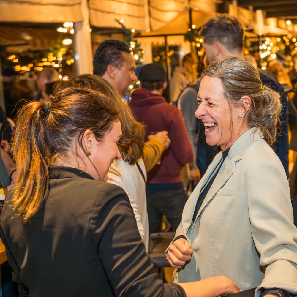 Twee vrouwen die lachen en praten op een kerstborrel met kerstmarkt met sfeerverlichting.