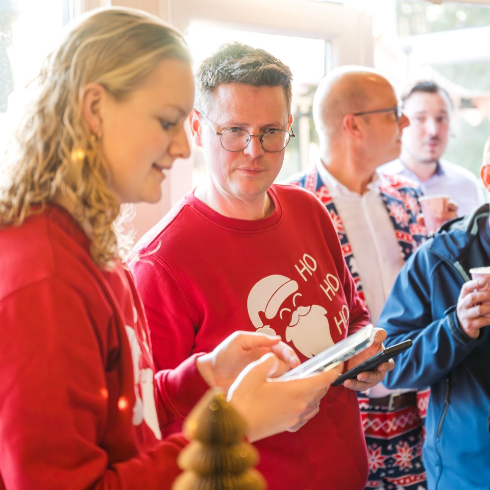 Organisatie en team van Pop-up Kerstmarkt met feestelijke kersttruien, een man in het midden draagt een rode trui met een kerstman en 'HO HO HO'.