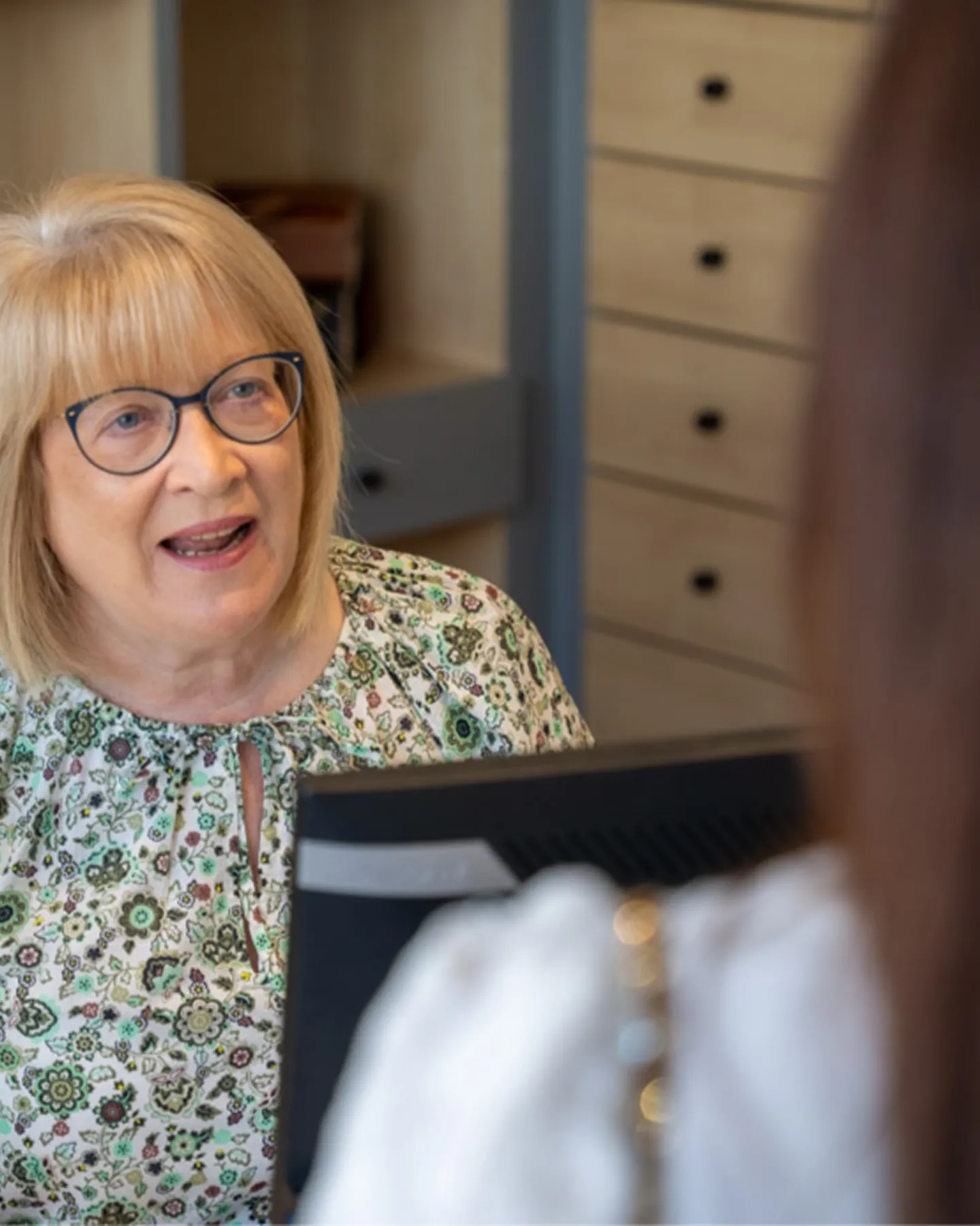Female patient wearing glasses speaking with optician receptionist during appointment booking at independent opticians