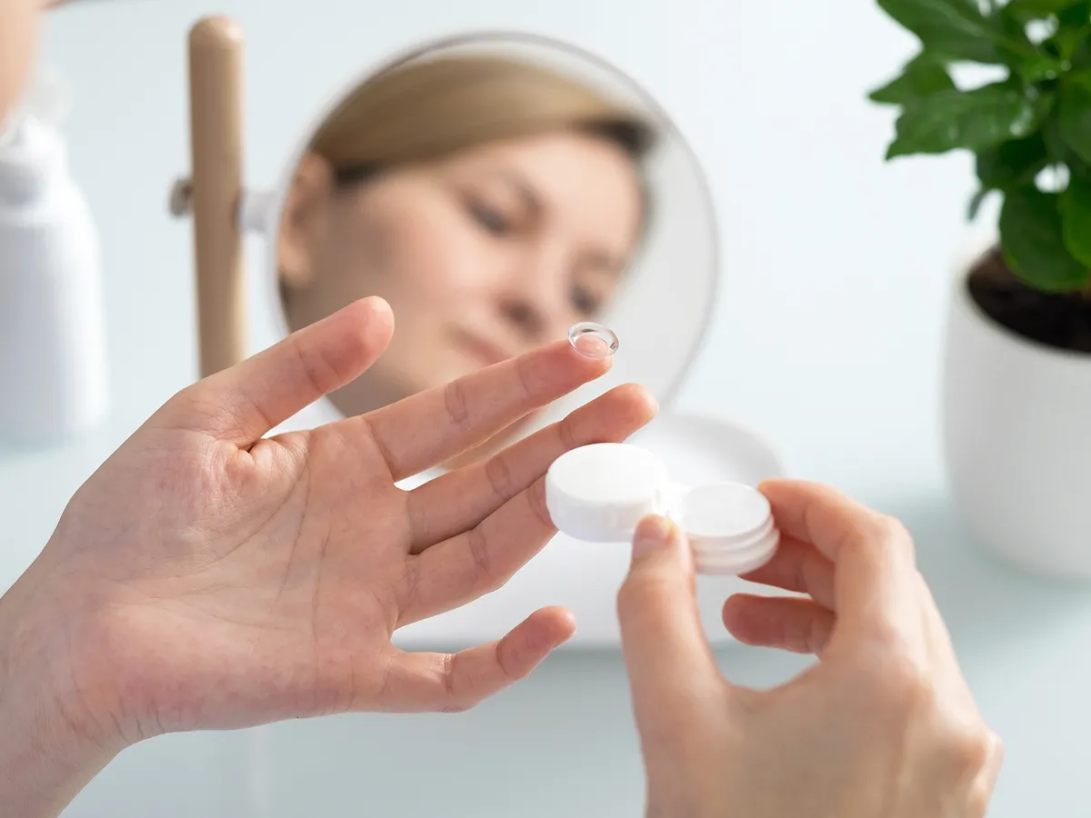 Woman removing a contact lens from its storage case in front of a mirror