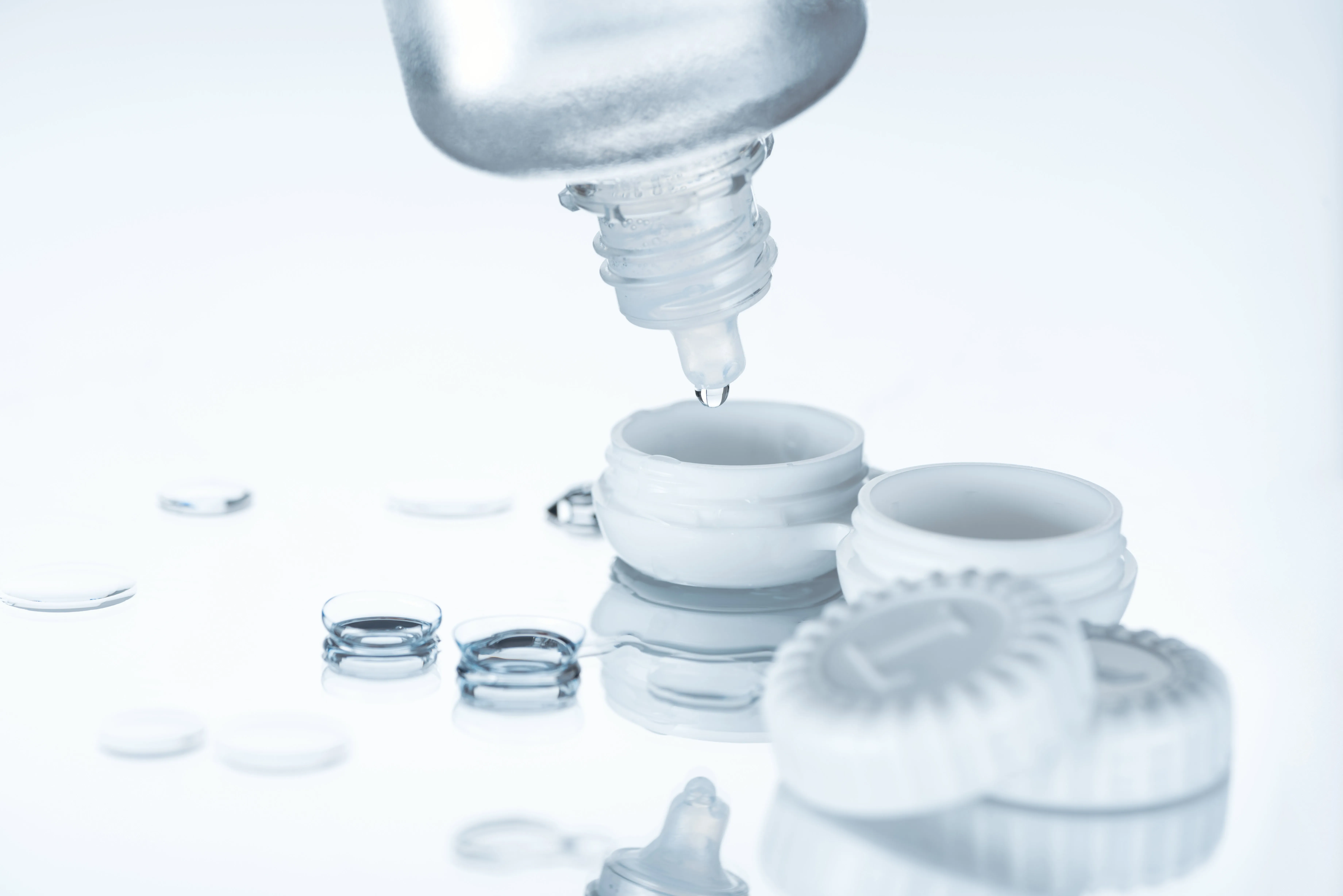 Contact lens solution being poured into a storage case alongside multiple contact lenses for cleaning and aftercare