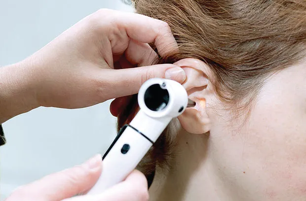 Clinician using an otoscope to examine a patient's ear during an ear wax removal consultation