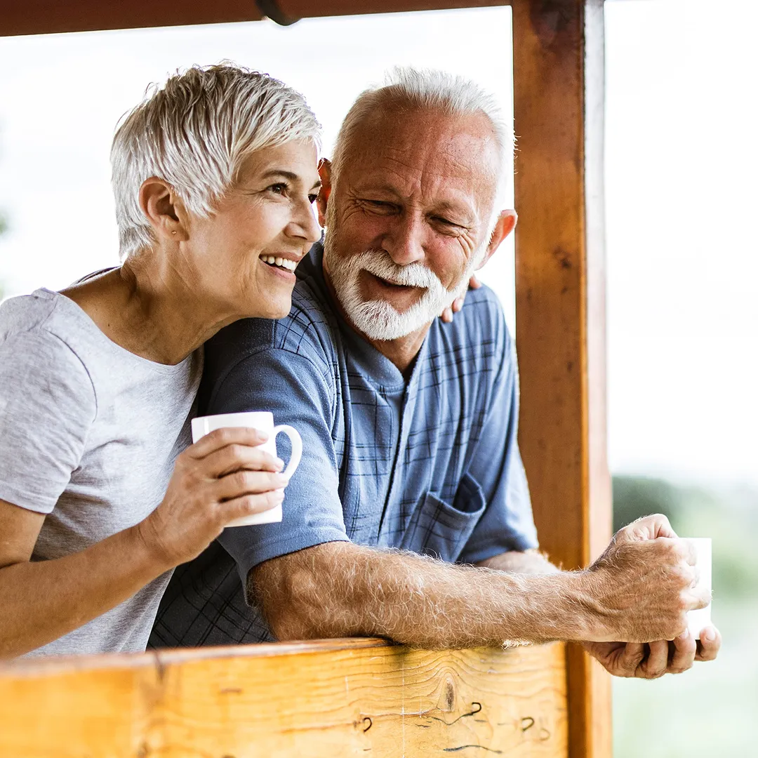 Happy mature couple relaxing on a balcony with coffee, enjoying life with improved hearing care