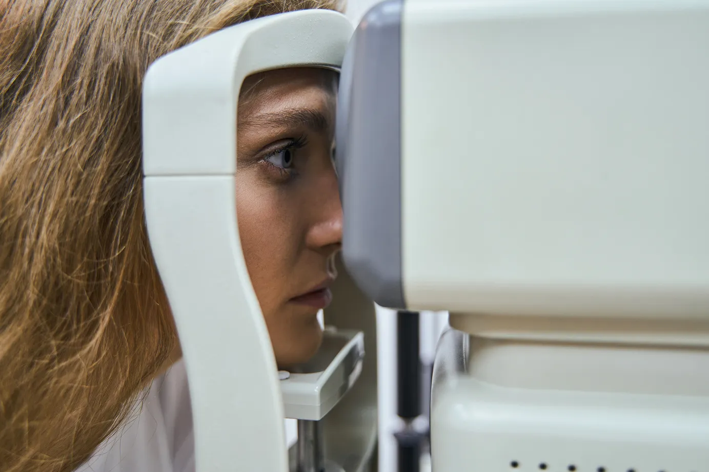 Close-up of a woman undergoing an eye exam using optical diagnostic equipment.