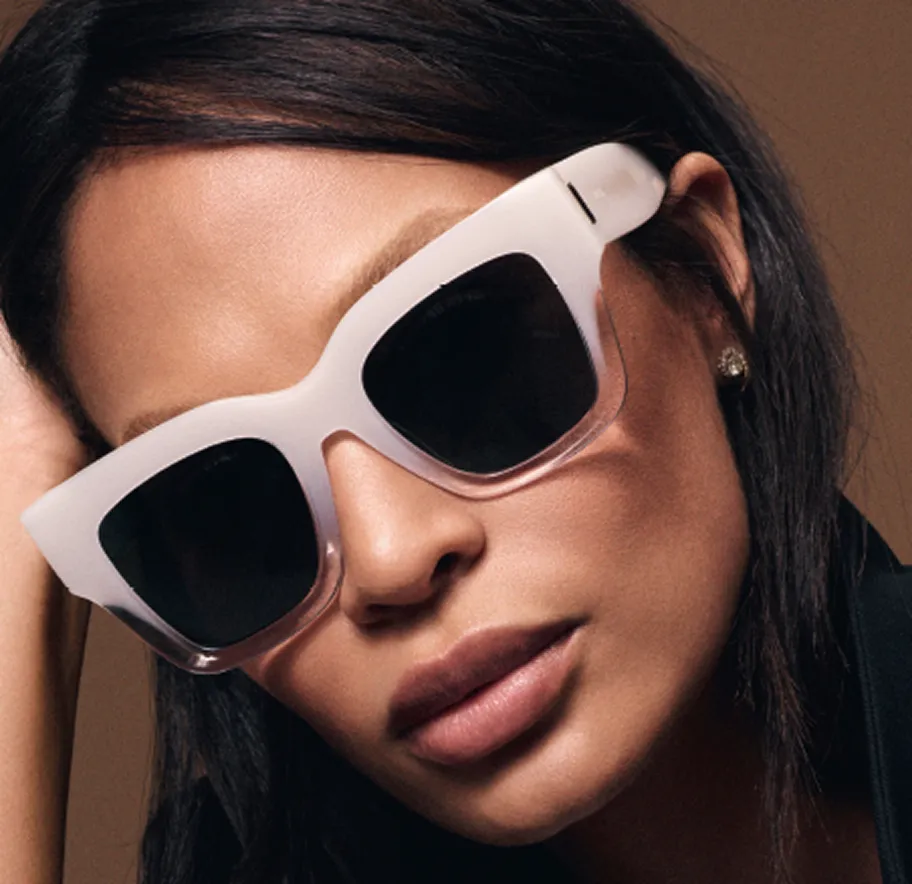 Close-up of a woman wearing large white-framed sunglasses and a black outfit.