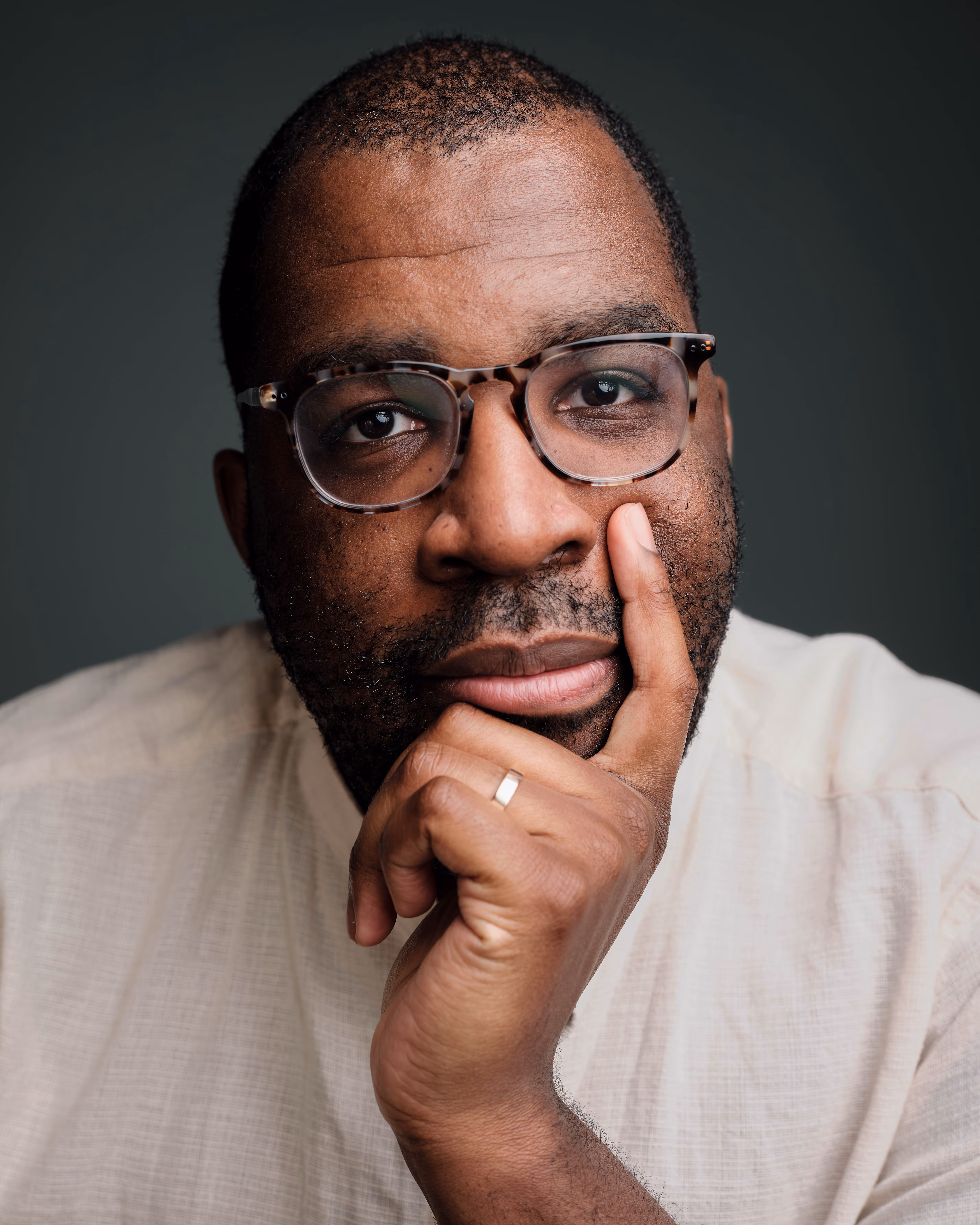 Close-up portrait of a man wearing glasses and a light shirt, thoughtful expression in studio lighting.