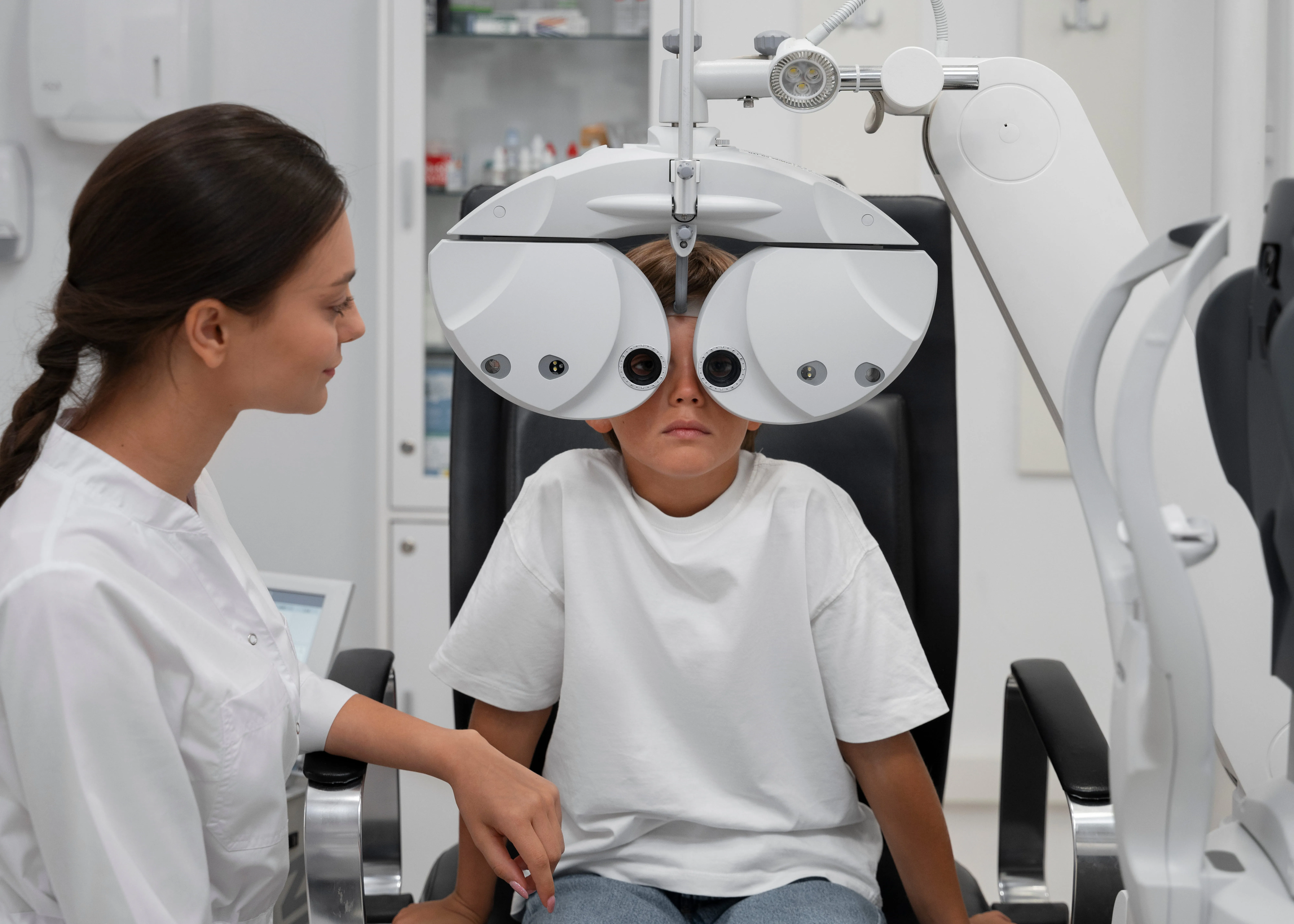 Female optometrist conducting eye examination on young patient using phoropter in clinical setting