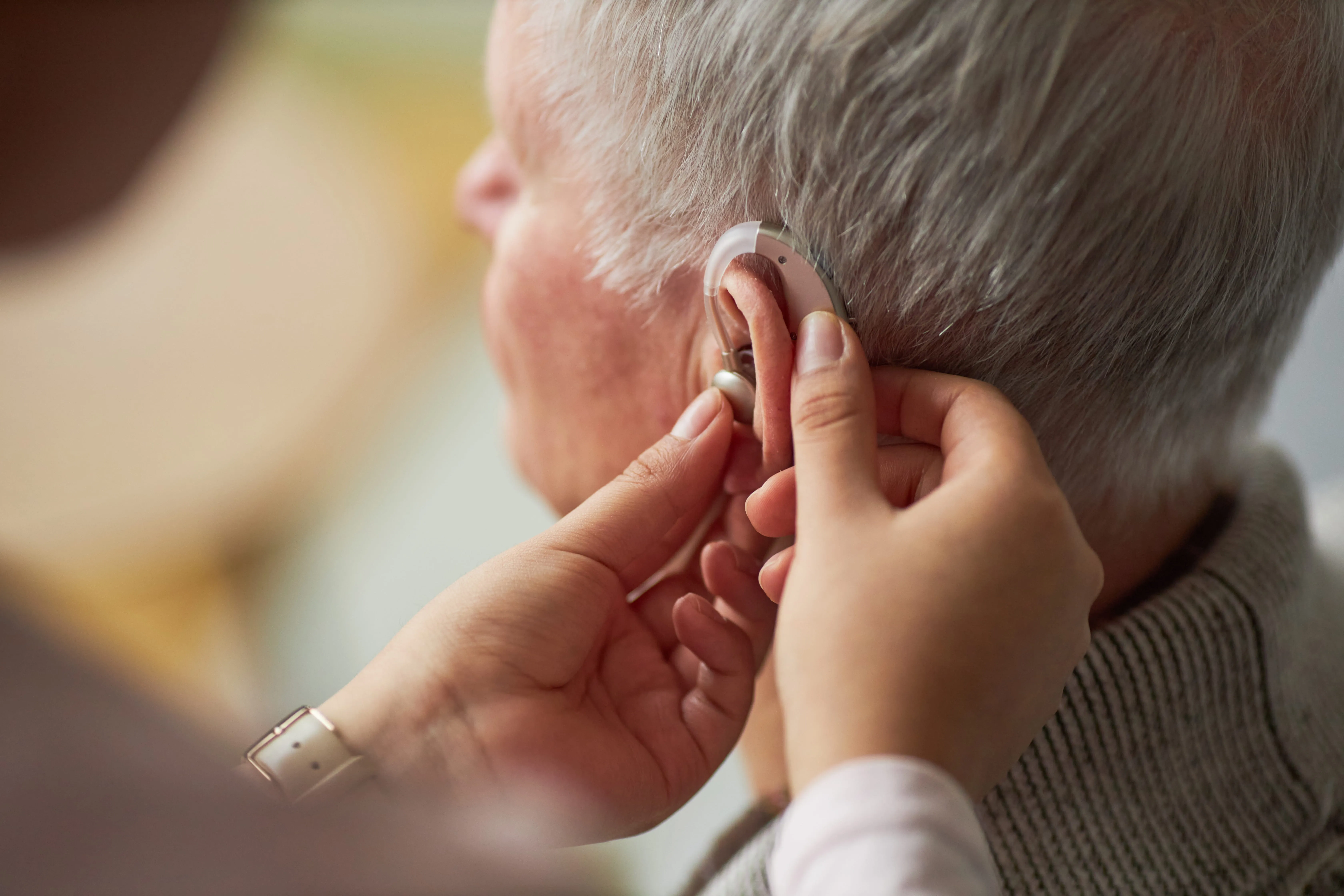 Child's hand adjusting hearing aid on elderly person's ear closely