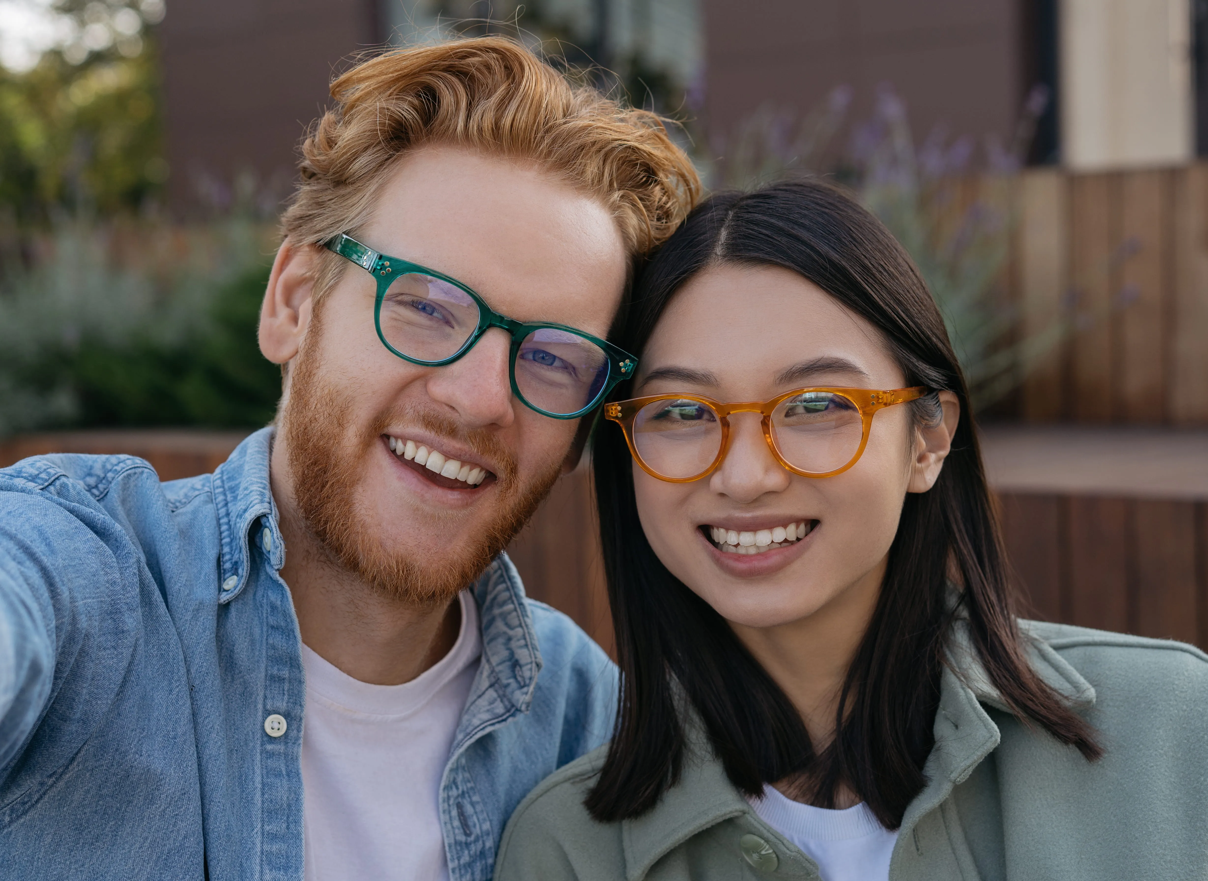 Two smiling young people wearing eyeglasses posing together outdoors for a portrait