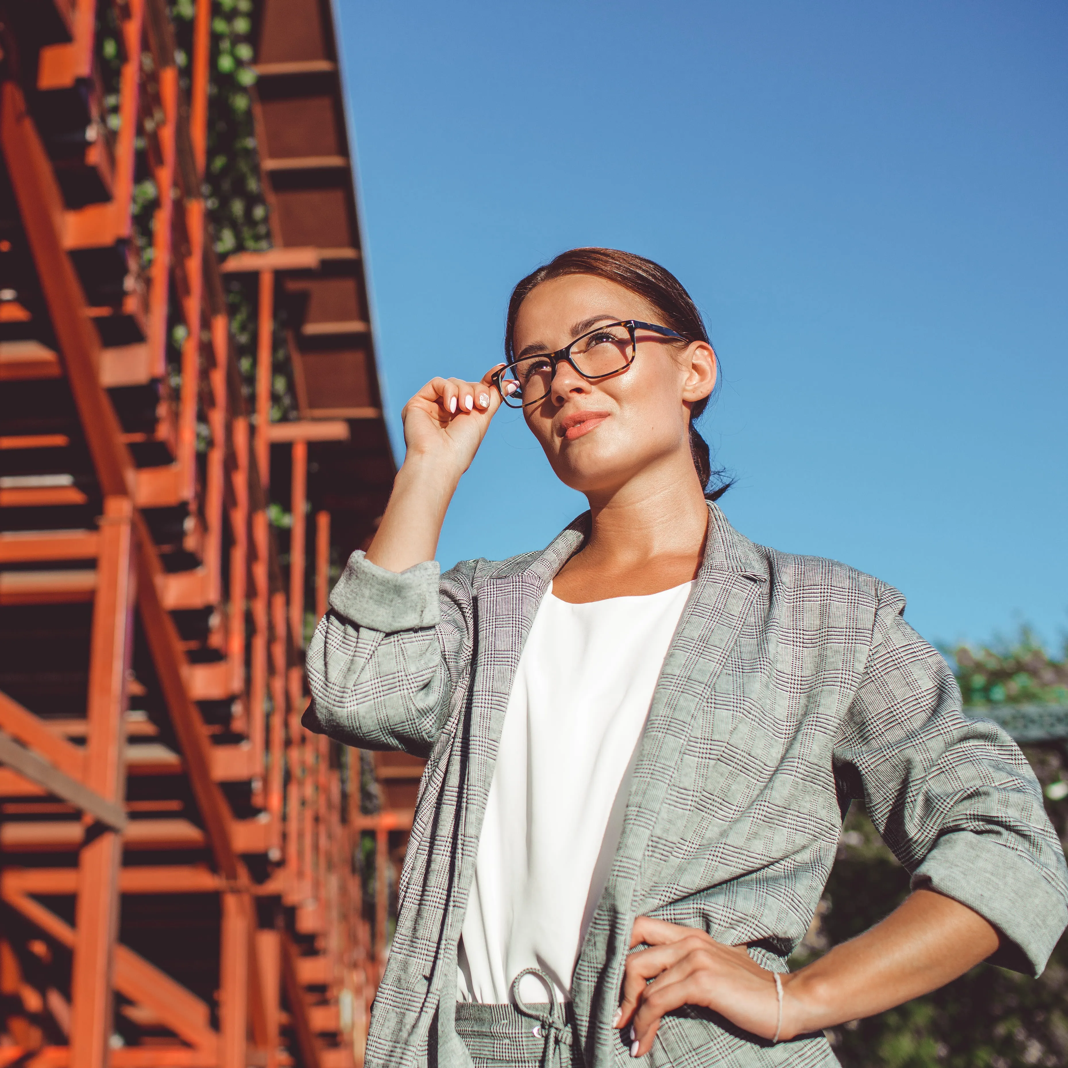 Woman in plaid blazer and glasses standing near orange structural metal framework