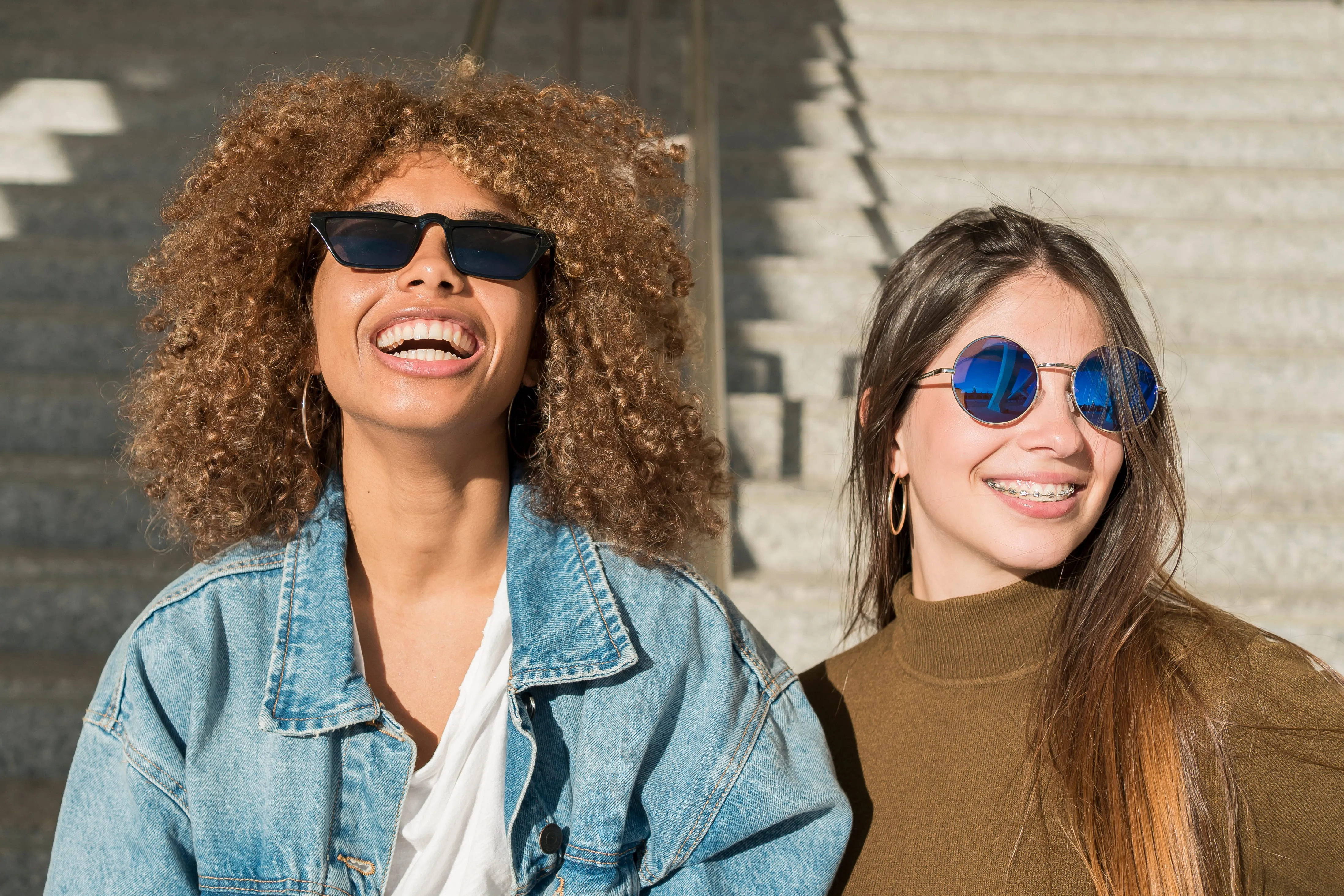 Two smiling women wearing sunglasses outdoors in urban setting
